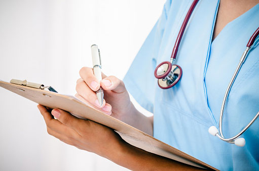 Close up image of a nurse filling out paperwork on a clipboard